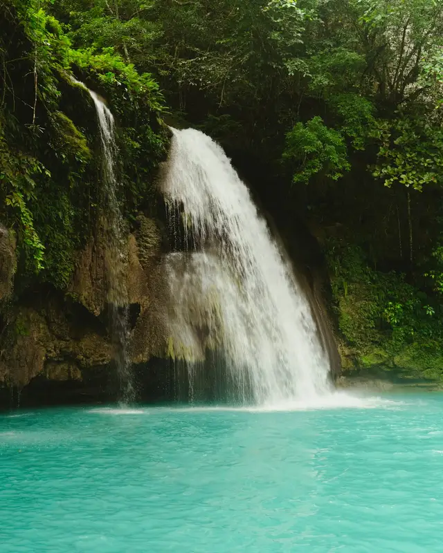 A waterfall pouring into a bright turquoise pool ringed by jungle