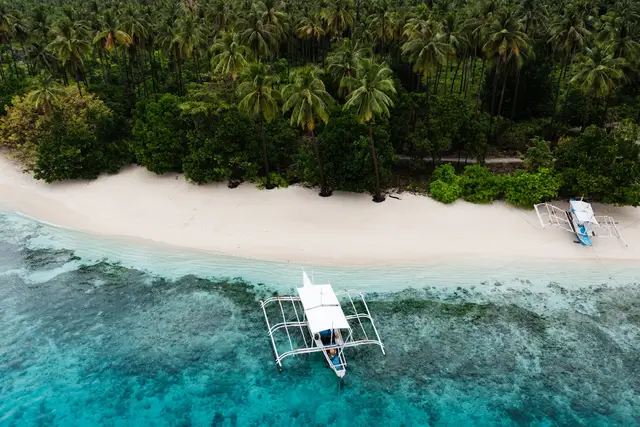 An outrigger banca floating at the reef edge off a palm-lined white beach