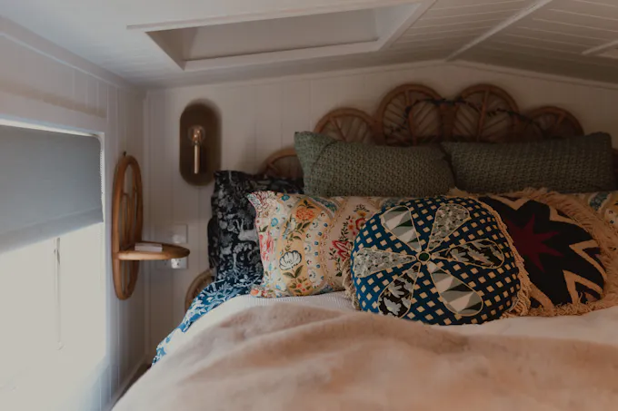 A bed with a woven rattan headboard and patterned pillows beside a bright window