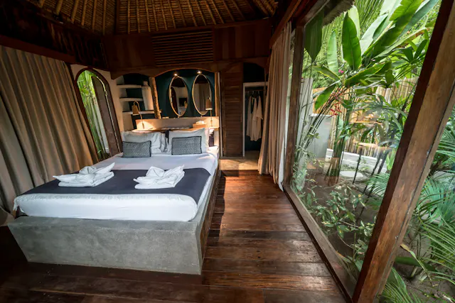 A bedroom with a low platform bed and full-height windows looking into dense garden plants