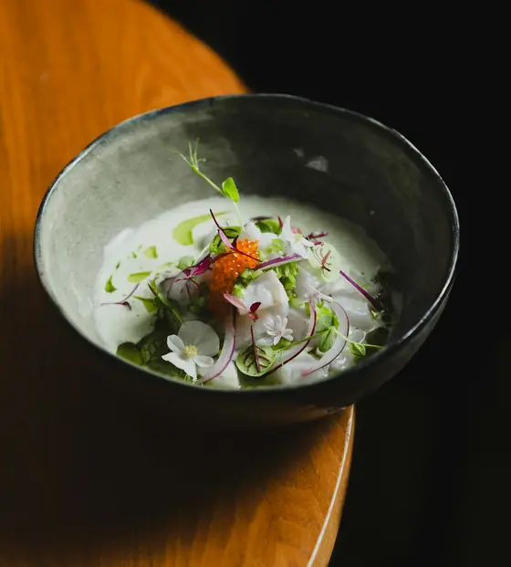 A dark ceramic bowl of raw fish dressed with onions, herbs and roe on a wooden table