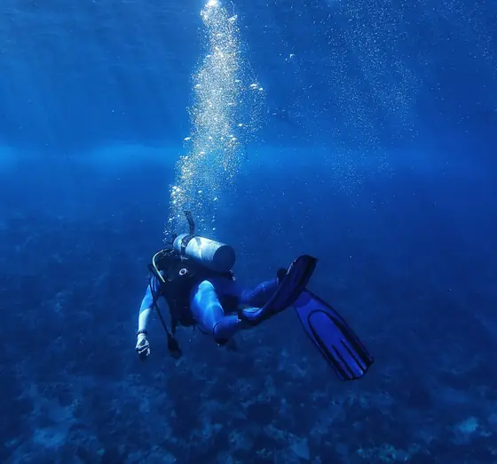 A scuba diver hanging in deep blue water, a column of bubbles rising above